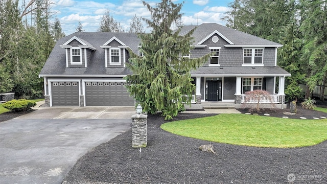 view of front facade with a shingled roof, a front yard, covered porch, and driveway