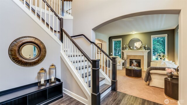 stairs with arched walkways, wood finished floors, baseboards, and a premium fireplace