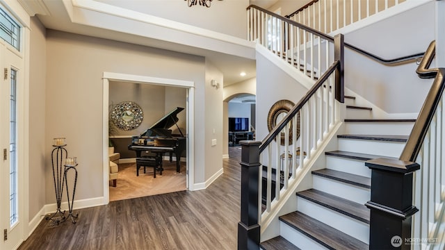 foyer entrance featuring dark wood-style floors, a high ceiling, baseboards, and arched walkways