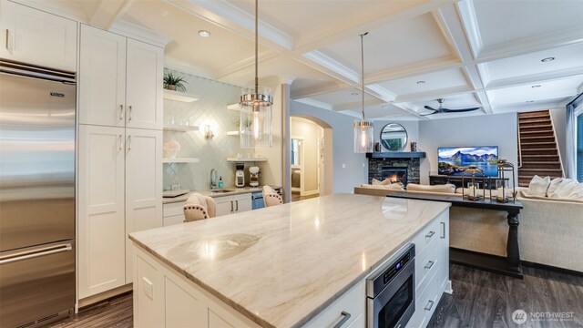 kitchen featuring built in appliances, a stone fireplace, dark wood-type flooring, coffered ceiling, and open floor plan