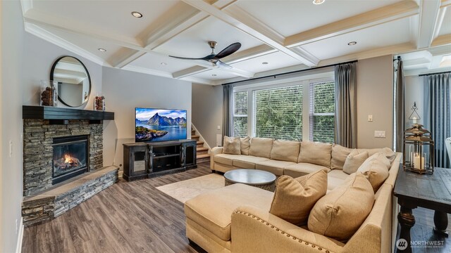 living room featuring beamed ceiling, coffered ceiling, wood finished floors, and a stone fireplace