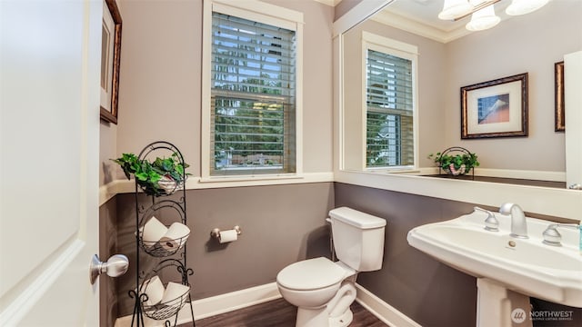 half bath featuring crown molding, toilet, a sink, wood finished floors, and baseboards