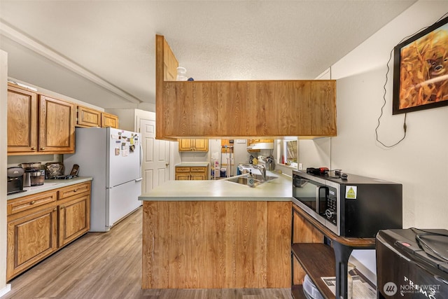 kitchen featuring a peninsula, stainless steel microwave, light countertops, and freestanding refrigerator