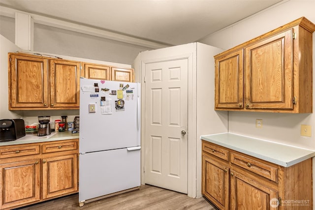 kitchen featuring brown cabinets, freestanding refrigerator, light countertops, and light wood-style floors