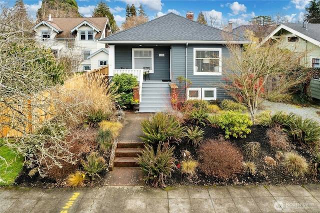 bungalow-style house with a shingled roof, a chimney, and a porch