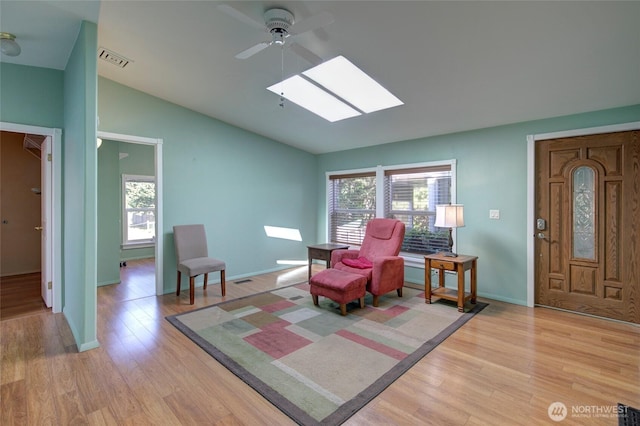 sitting room featuring vaulted ceiling with skylight, light wood-style flooring, plenty of natural light, and visible vents