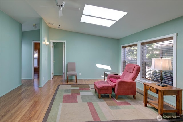 living area featuring light wood-style floors, vaulted ceiling with skylight, visible vents, and baseboards