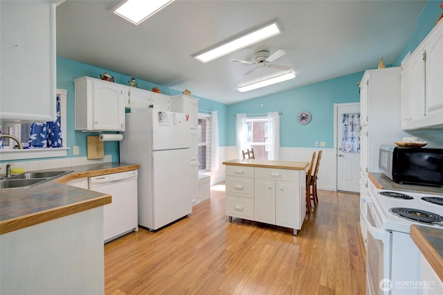 kitchen with white appliances, a sink, white cabinets, vaulted ceiling, and light wood finished floors