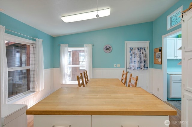 dining space featuring vaulted ceiling and wainscoting