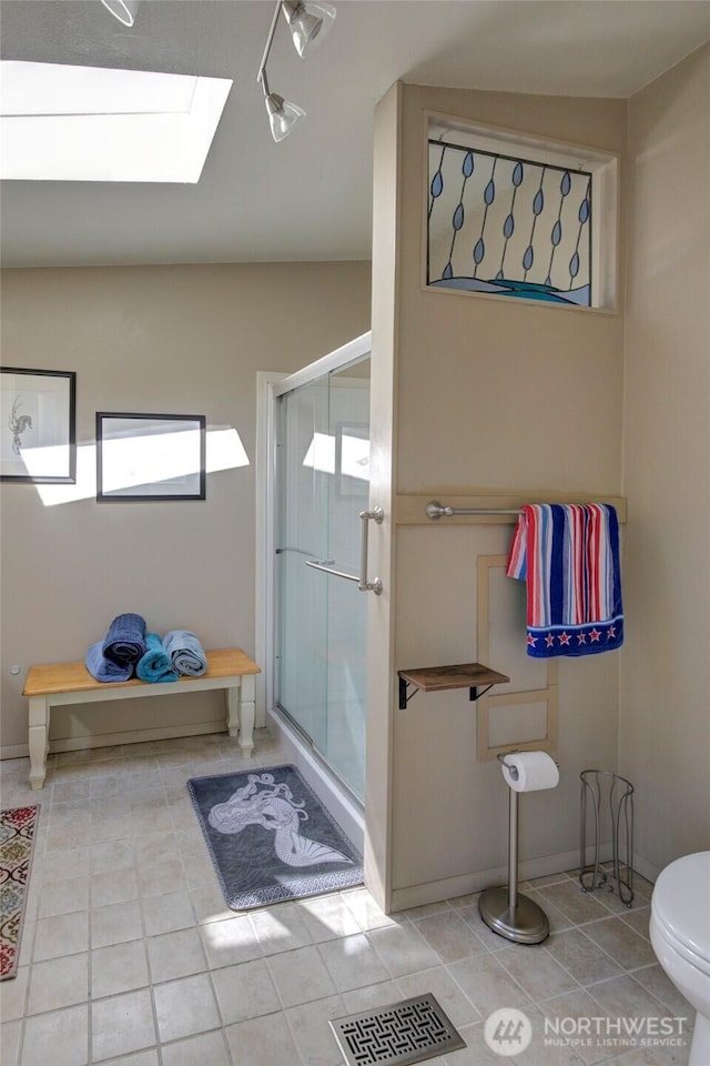 bathroom with a skylight, a stall shower, visible vents, toilet, and tile patterned flooring