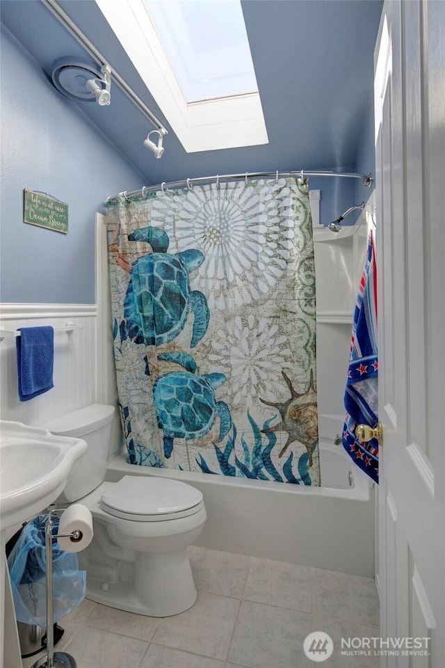 full bathroom featuring tile patterned flooring, toilet, a wainscoted wall, a skylight, and shower / bathtub combination with curtain