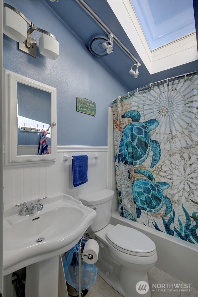 bathroom with a skylight, shower / bath combo, wainscoting, toilet, and a sink