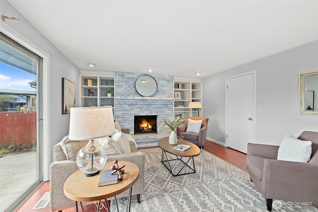 living room with hardwood / wood-style flooring, built in shelves, and a fireplace