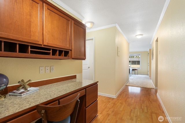 kitchen with light wood finished floors, brown cabinetry, built in study area, light stone counters, and crown molding