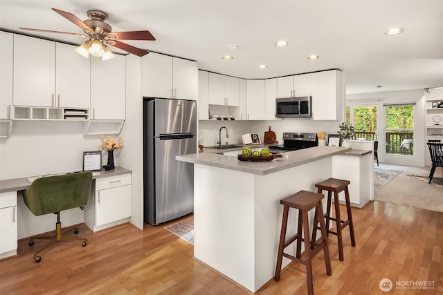 kitchen with a sink, white cabinetry, light wood-style floors, a kitchen breakfast bar, and appliances with stainless steel finishes