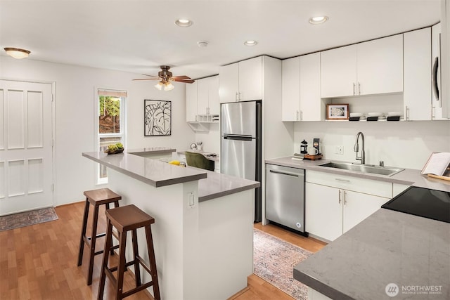 kitchen with stainless steel appliances, a breakfast bar, white cabinetry, and a sink