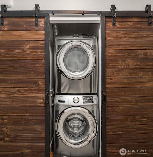 laundry area with stacked washer and dryer, a barn door, and laundry area