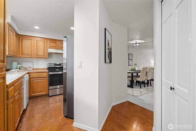 kitchen featuring light wood-style flooring, stainless steel appliances, light countertops, under cabinet range hood, and recessed lighting