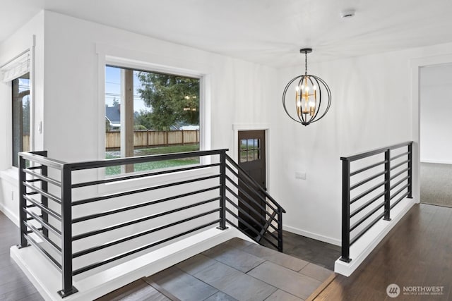 staircase with wood finished floors, baseboards, and an inviting chandelier