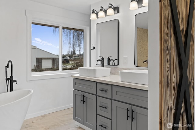 full bathroom featuring double vanity, a freestanding tub, a sink, and baseboards