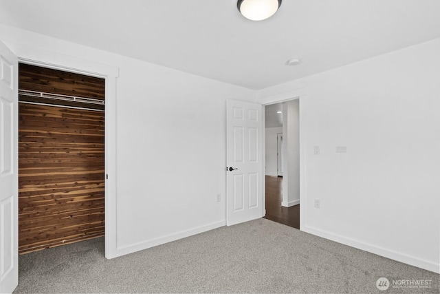 unfurnished bedroom featuring carpet floors, wood walls, baseboards, and a closet