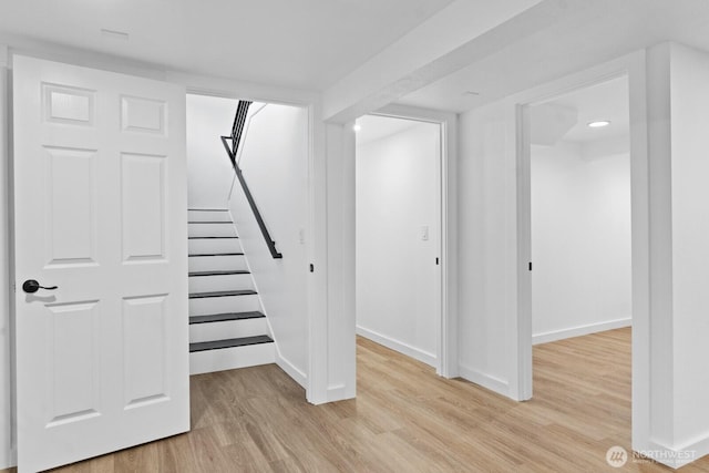 below grade area featuring stairs, light wood-style flooring, and baseboards