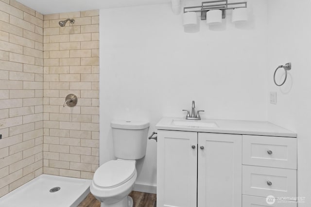 bathroom with toilet, a stall shower, vanity, wood finished floors, and baseboards