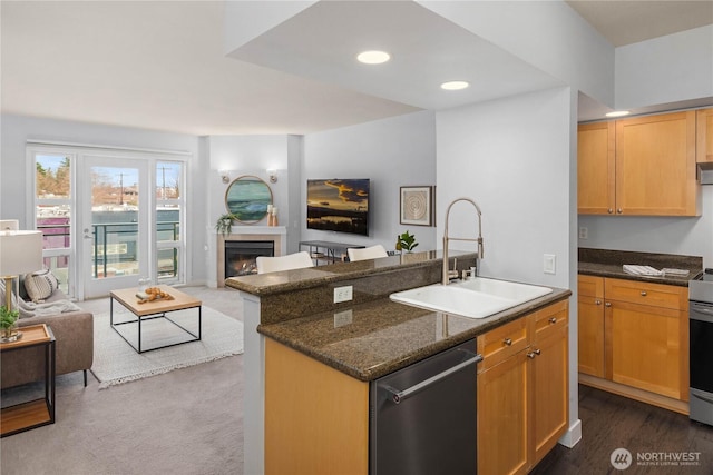 kitchen with a sink, open floor plan, dark stone counters, a glass covered fireplace, and dishwasher