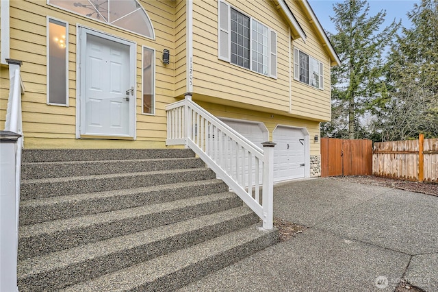 view of exterior entry with a garage, driveway, and fence