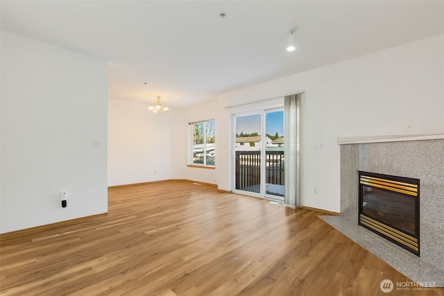 unfurnished living room featuring a notable chandelier, a fireplace, light wood-style flooring, and baseboards