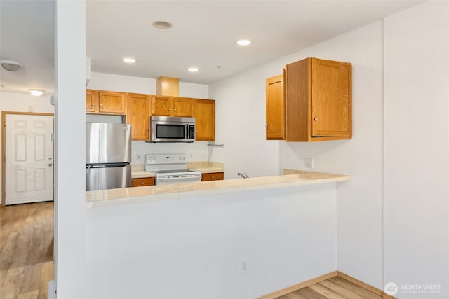 kitchen with a peninsula, light wood finished floors, stainless steel appliances, and light countertops