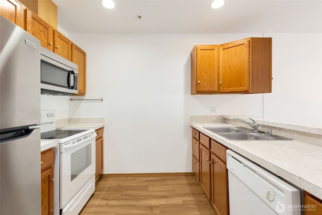 kitchen with light wood finished floors, brown cabinetry, appliances with stainless steel finishes, light countertops, and a sink