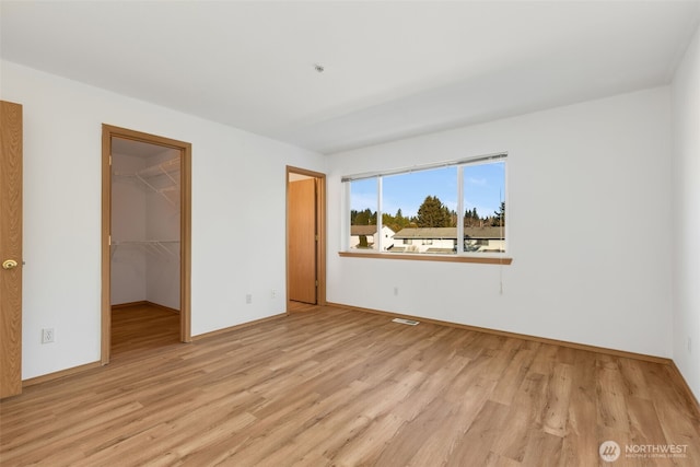 unfurnished bedroom with a walk in closet, a closet, and light wood-style flooring