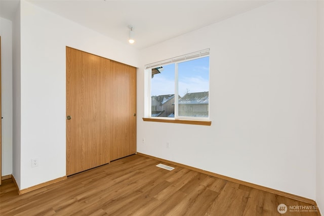 unfurnished bedroom with a closet, light wood-type flooring, visible vents, and baseboards