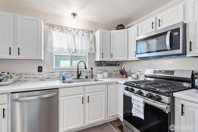 kitchen with stainless steel appliances, a textured ceiling, light countertops, white cabinetry, and a sink