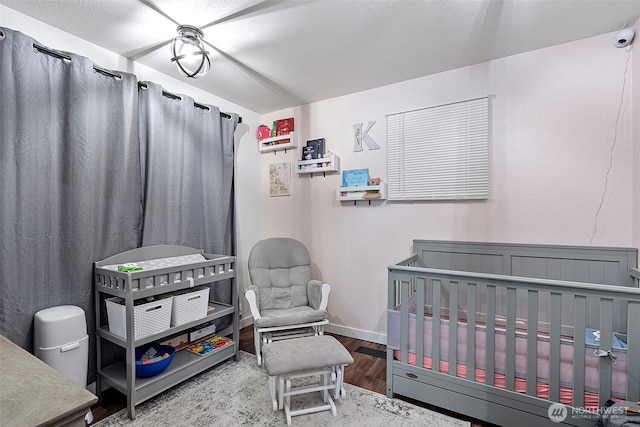 bedroom with a nursery area, baseboards, and wood finished floors