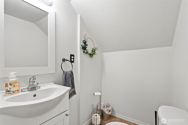 half bath with a textured wall, vaulted ceiling, a textured ceiling, and vanity