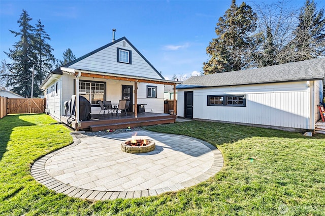 back of property featuring a deck, an outbuilding, an outdoor fire pit, fence, and a lawn