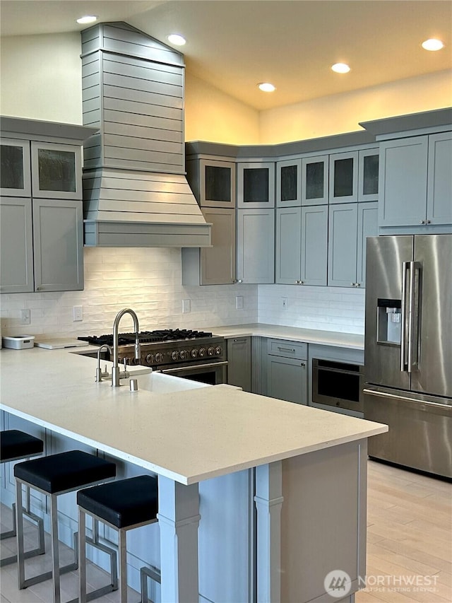 kitchen with tasteful backsplash, high end appliances, light hardwood / wood-style floors, a breakfast bar, and sink