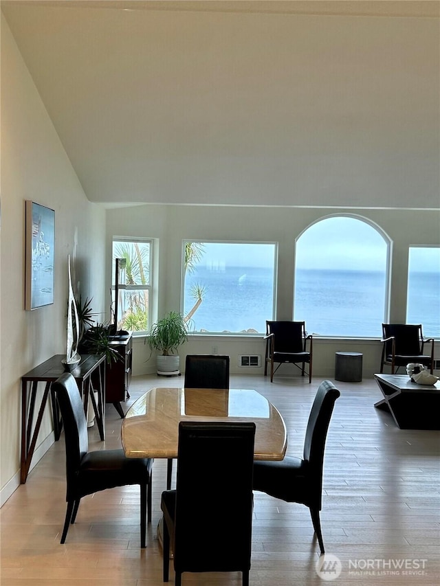 dining space featuring high vaulted ceiling, a water view, and light hardwood / wood-style floors