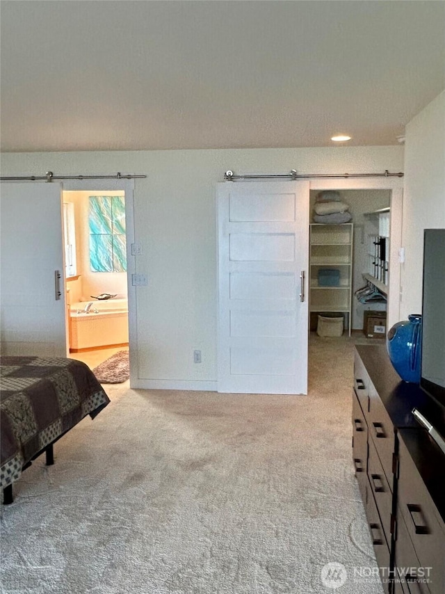 bedroom with light carpet, ensuite bathroom, and a barn door