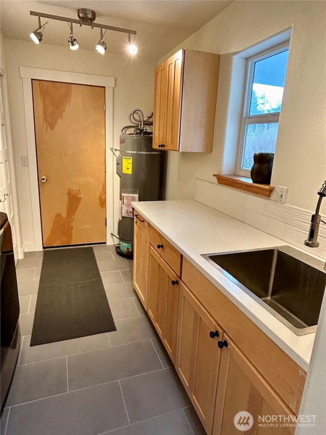 kitchen with sink, dark tile patterned flooring, light brown cabinets, and strapped water heater