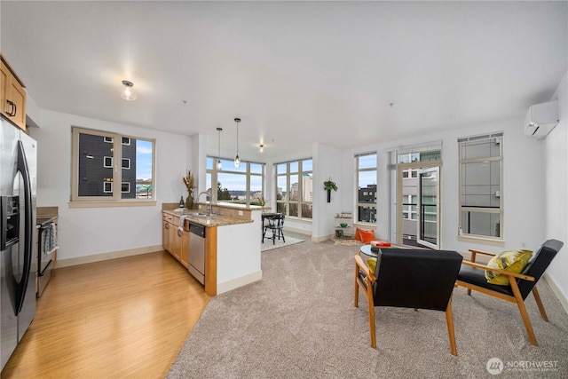 kitchen featuring stainless steel appliances, a sink, hanging light fixtures, a wall mounted AC, and light stone countertops