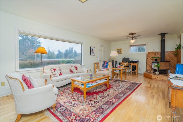 living area with a wood stove, ceiling fan, and wood finished floors