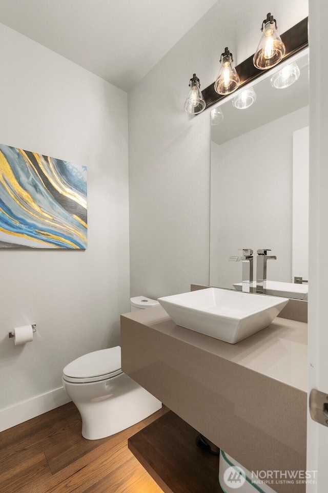 half bath featuring toilet, baseboards, a sink, and wood finished floors