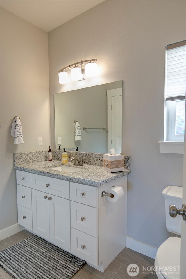 half bath featuring toilet, baseboards, wood finished floors, and vanity