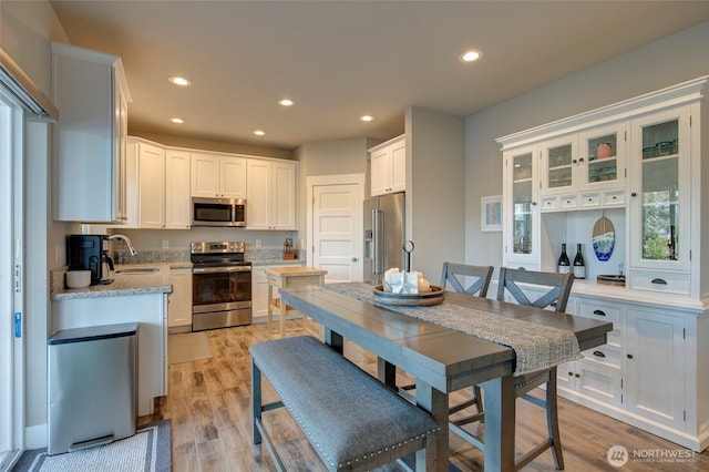 kitchen featuring appliances with stainless steel finishes, a sink, light wood-style floors, and white cabinets