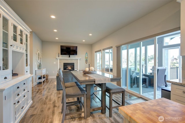 dining room with light wood-type flooring, recessed lighting, baseboards, and a glass covered fireplace