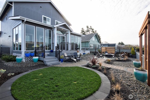 rear view of property with a patio, a lawn, an outdoor fire pit, a sunroom, and fence