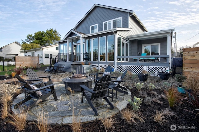 rear view of house with an outdoor fire pit, a patio area, fence, and a sunroom